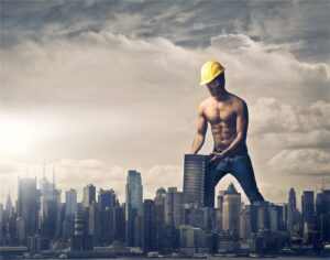 Shirtless builder in a hard hat standing on a skyscraper above a city skyline