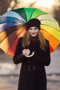 Smiling woman in a winter coat holding a rainbow umbrella