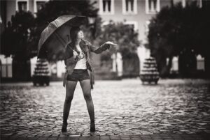 Black and white photo of a woman with an umbrella on a rainy cobblestone street